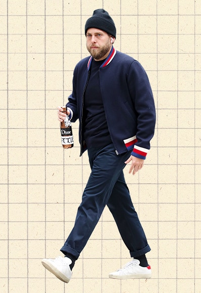 Outfit Of The Day #1,153 – Jonah Hill In New York Wearing Navy Blue Letterman Bomber Jacket, Blue T-Shirt, Straight-leg Chinos And White Leather Saint Laurent Trainers.