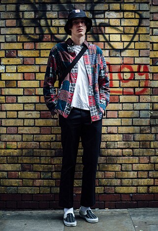 A street-styler at London Fashion Week Men's wearing a patchwork checked shirt, white tee, black trousers and patterned slip-on Vans | ASOS Style Feed