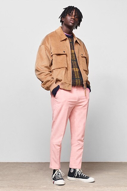 ASOS model wearing a tan corduroy jacket, gold jumper, pink trousers and black Converse trainers | ASOS Style Feed