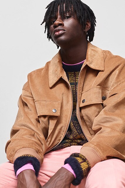 ASOS model wearing a tan corduroy jacket, gold jumper, pink trousers and black Converse trainers | ASOS Style Feed