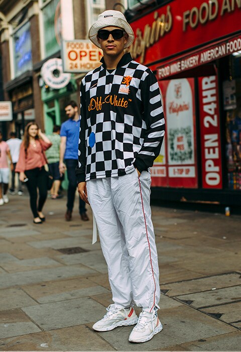 A street-styler at LFWM's SS19 wearing an Off-White football shirt, joggers, chunky trainers, a bucket hat and shades | ASOS Style Feed