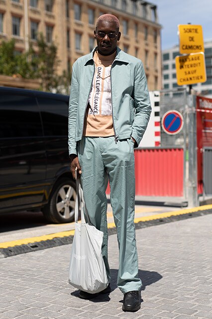 A street styler at Paris Fashion Week Men's SS19 wearing a colourful co-ord, sunglasses, a T-shirt and a tote bag | ASOS Style Feed