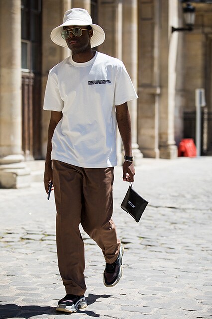 A street styler at Paris Fashion Week Men's SS19 wearing a cream T-shirt, brown trousers, a bucket hat, aviator shades and Balenciaga Triple S trainers | ASOS Style Feed