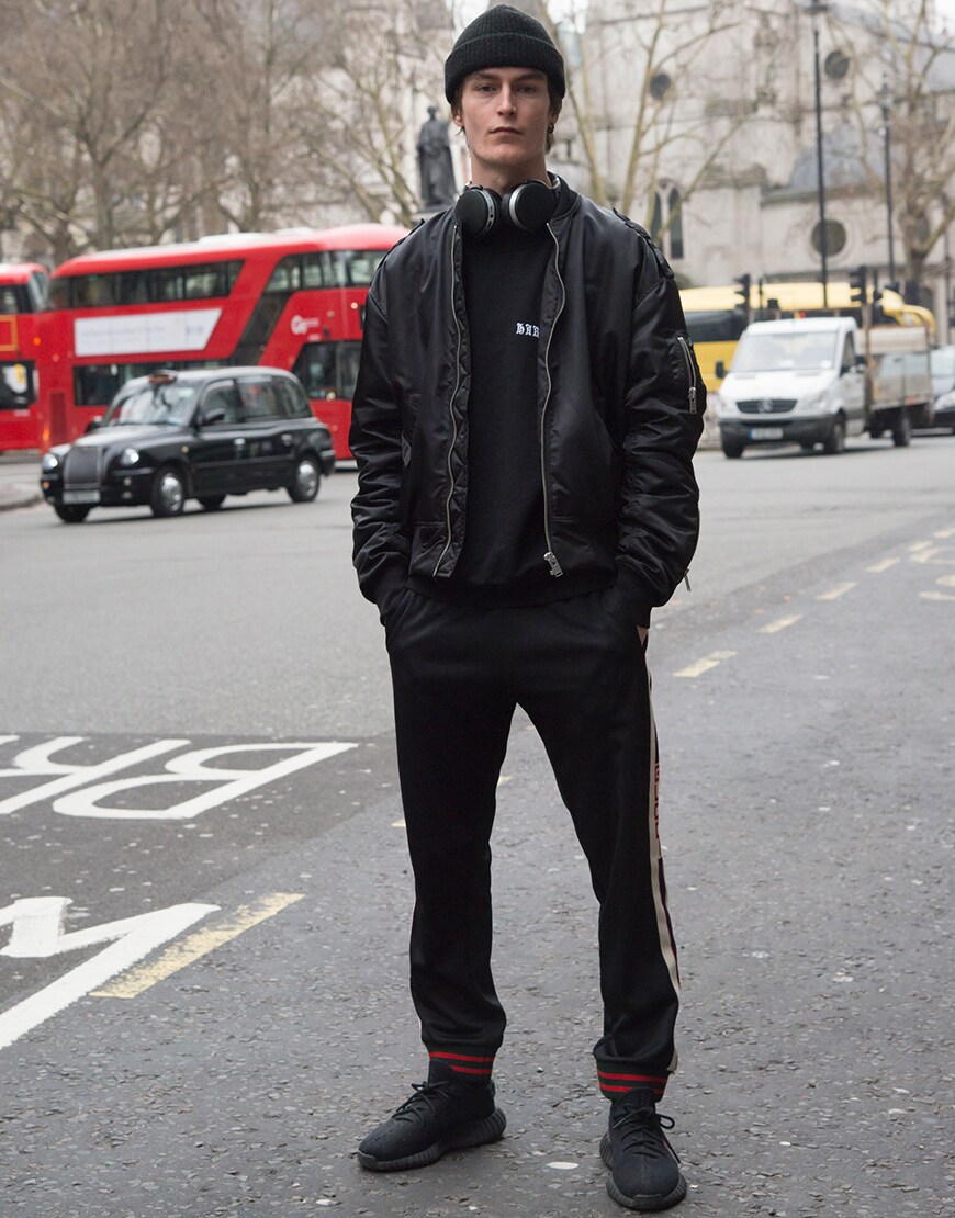 A street-styler wearing a black bomber jacket, sweatshirt, beanie, Yeezy trainers and side-stripe joggers | ASOS Style Feed