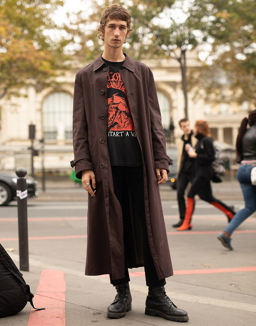 A street-styler wearing a graphic-print T-shirt, black jeans and a brown overcoat | ASOS Style Feed