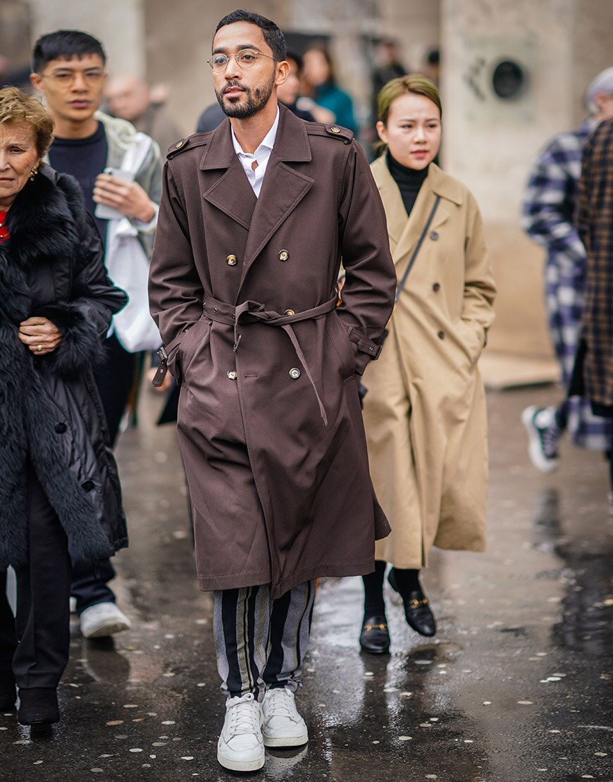 A street-styler wearing a shirt, brown trench coat, striped trousers and white trainers | ASOS Style Feed