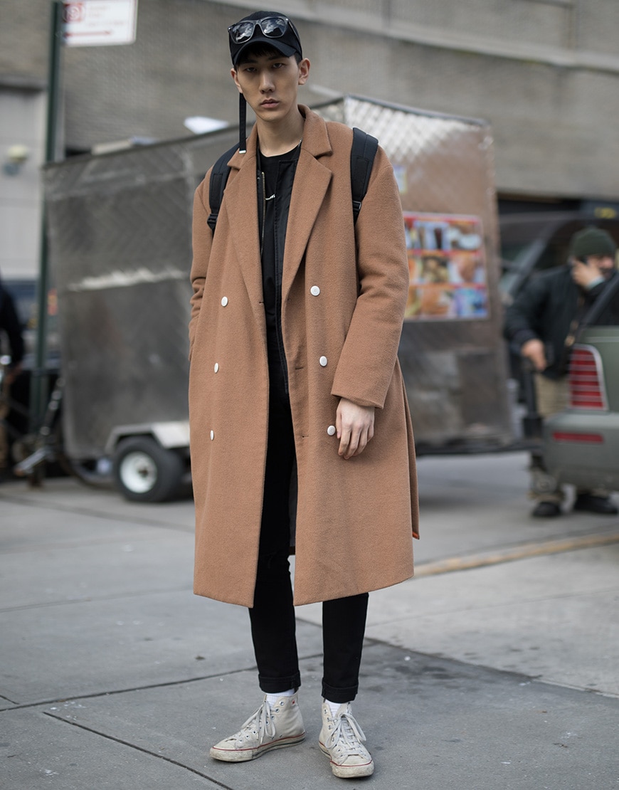 A street-styler wearing all black, a camel coat and Converse trainers | ASOS Style Feed