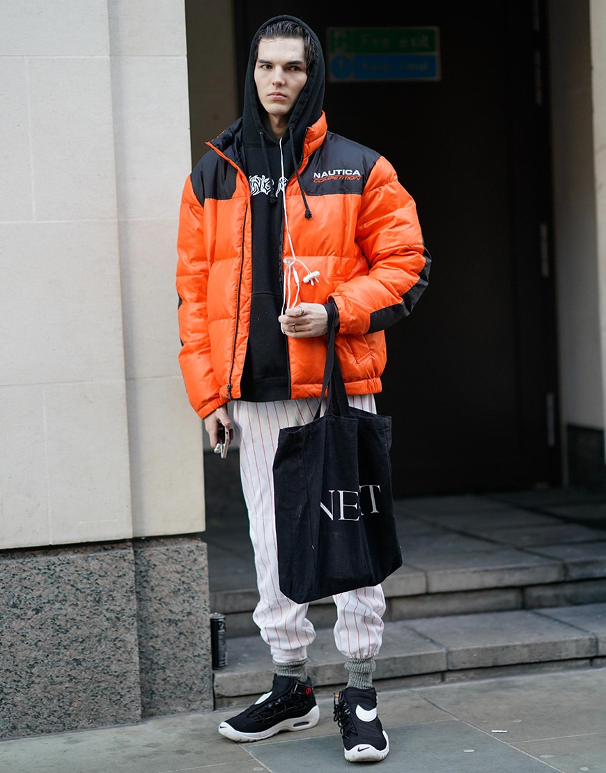 A street-styler wearing a hoodie, an emergency-orange puffers jacket, striped trousers and Nike trainers | ASOS Style Feed