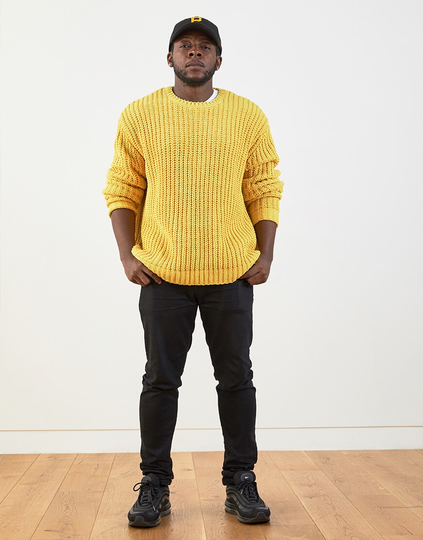 Charles wearing a yellow knitted jumper, black jeans, a black cap and black Air Max 97 trainers | ASOS Style Feed