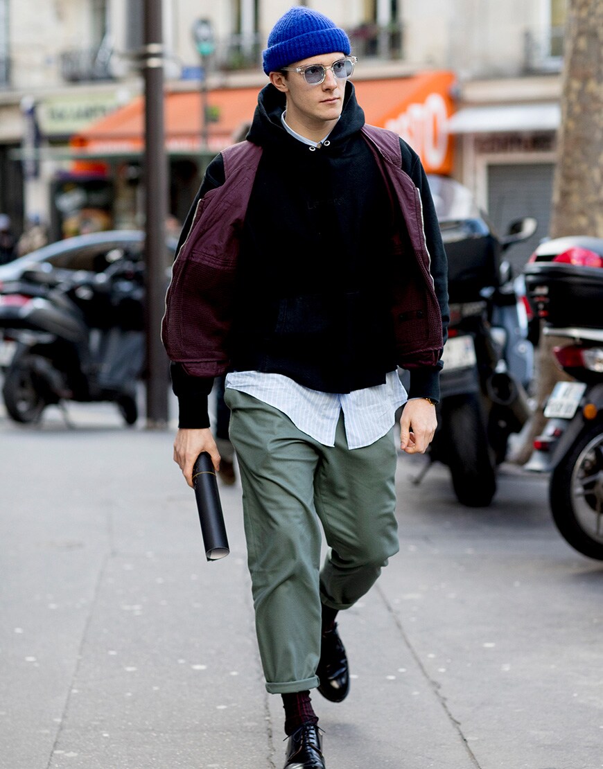 A man wearing a purple gilet with green chinos and a beanie