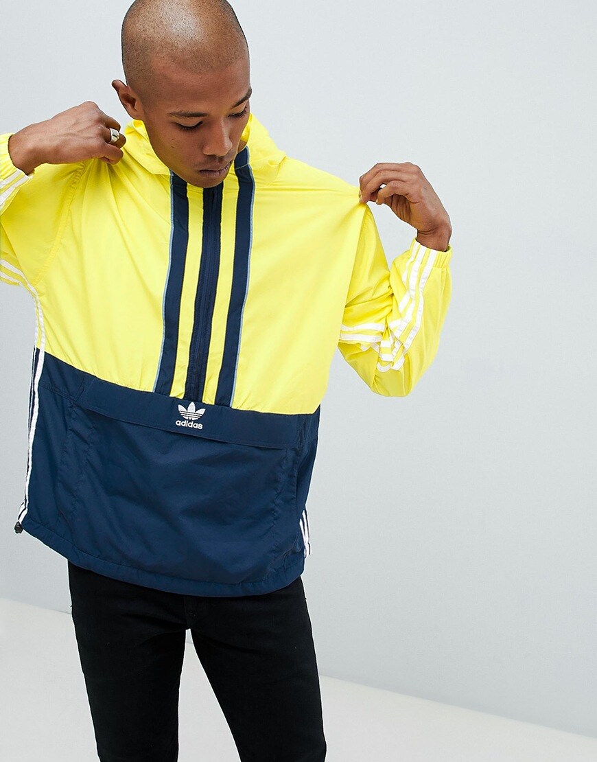 A picture of a model wearing a lightweight adidas windbreaker in yellow and navy. Available at ASOS