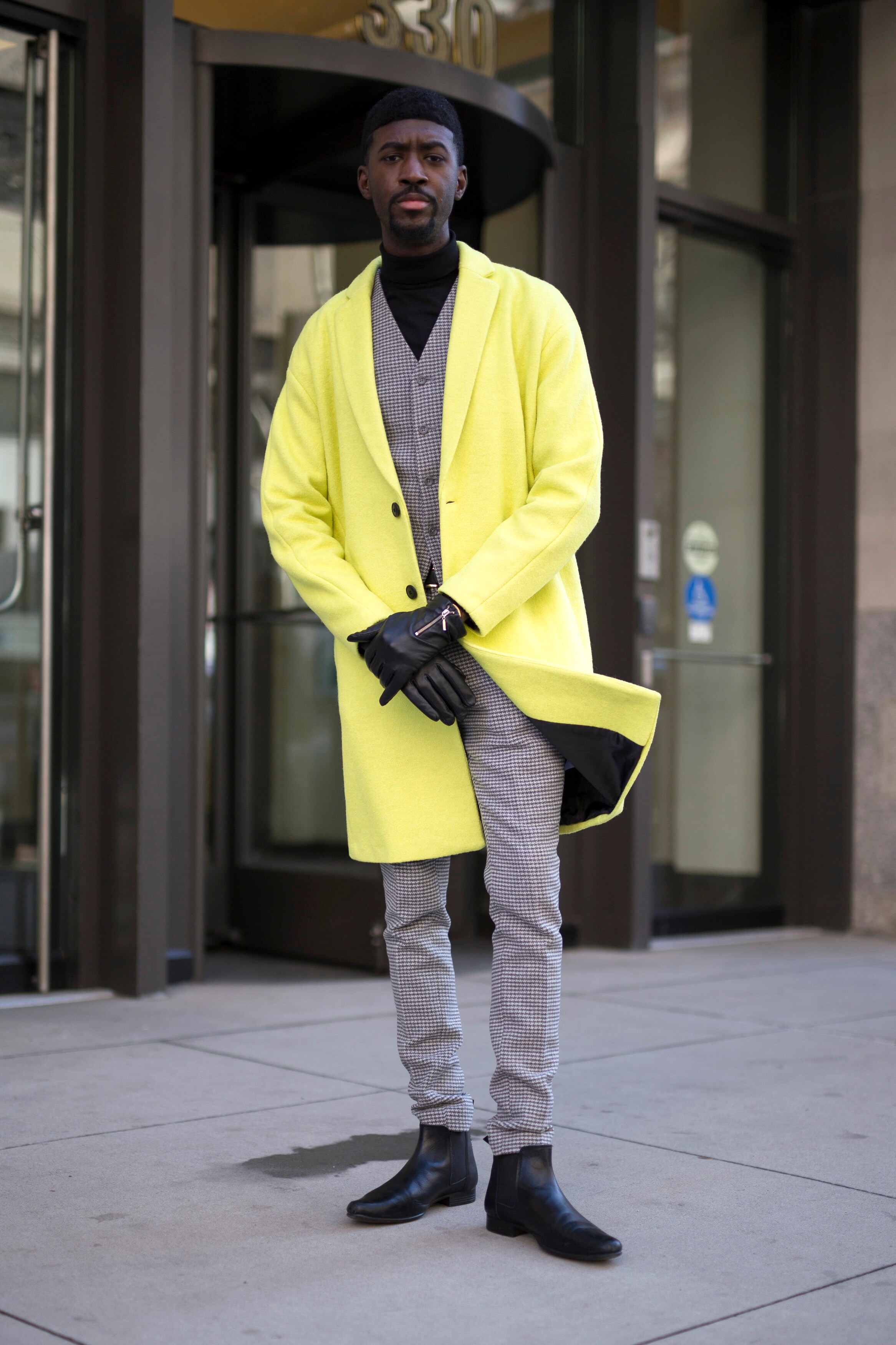 A streetstyler wearing a neon overcoat, a plain black roll neck, check suit and Chelsea boots