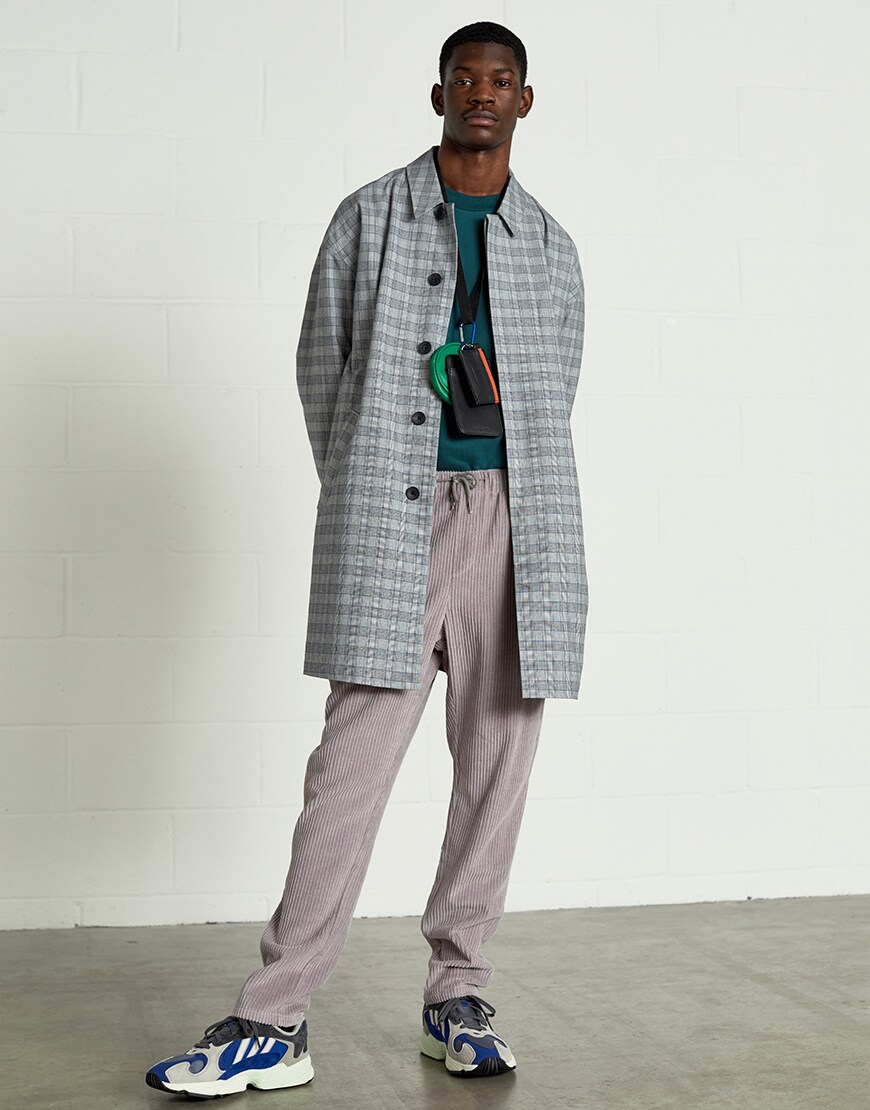 A picture of a model wearing an ASOS White outfit including a checked mac, corduroy trousers and adidas trainers