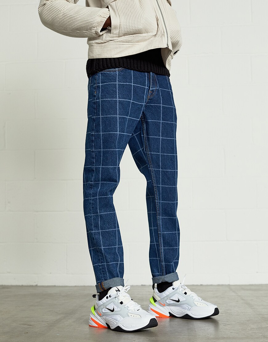 A picture of a model wearing an ASOS White outfit including a zip-through jacket, a black roll neck jumper and grid print jeans