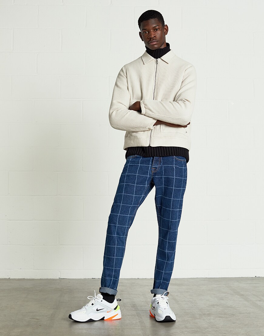 A picture of a model wearing an ASOS White outfit including a zip-through jacket, a black roll neck jumper and grid print jeans