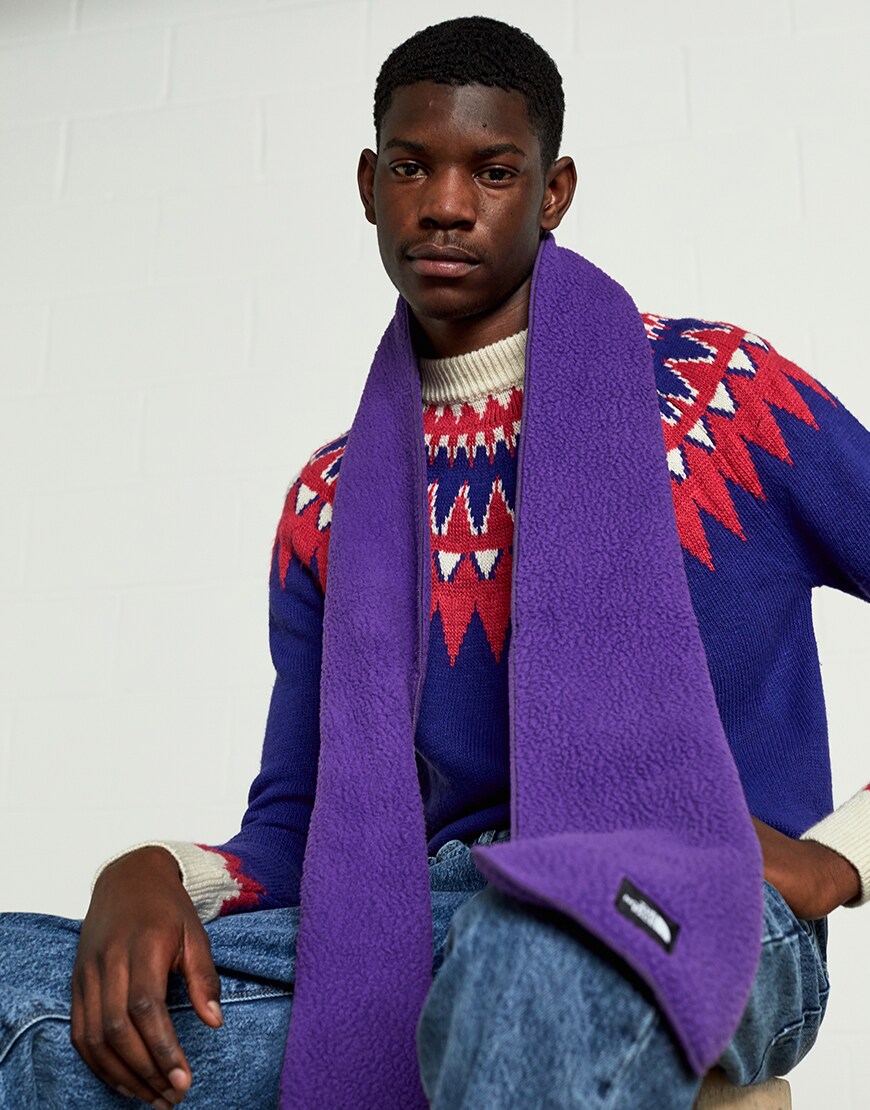 A picture of a man wearing a fleece scarf from The North Face, a knitted jumper and blue jeans. Available at ASOS