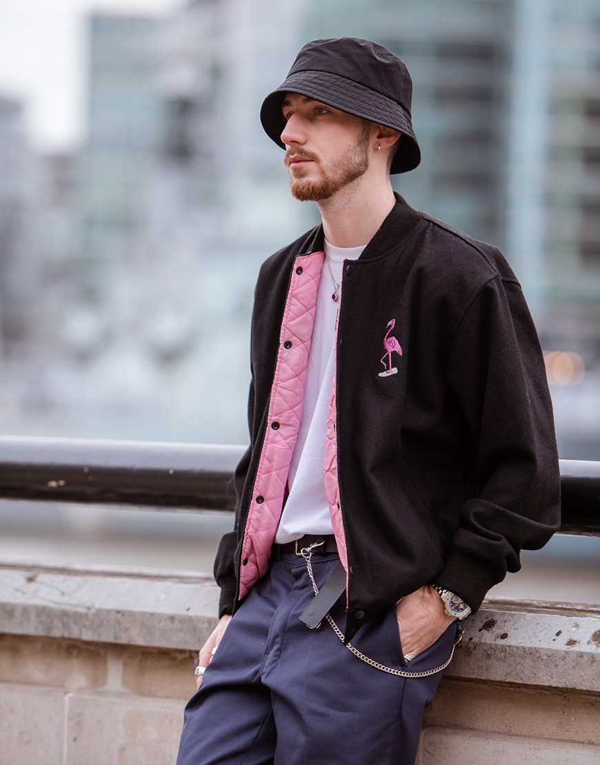 London street-styler wearing a black bucket hat, black bomber jacket with pink details and blue-grey work pants | ASOS Style Feed