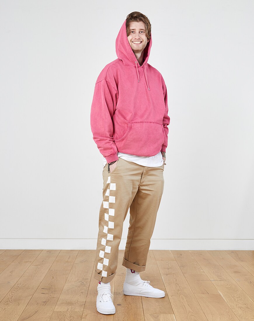 A picture of a man wearing a washed-pink hoodie, beige chinos with checkerboard details and white trainers.