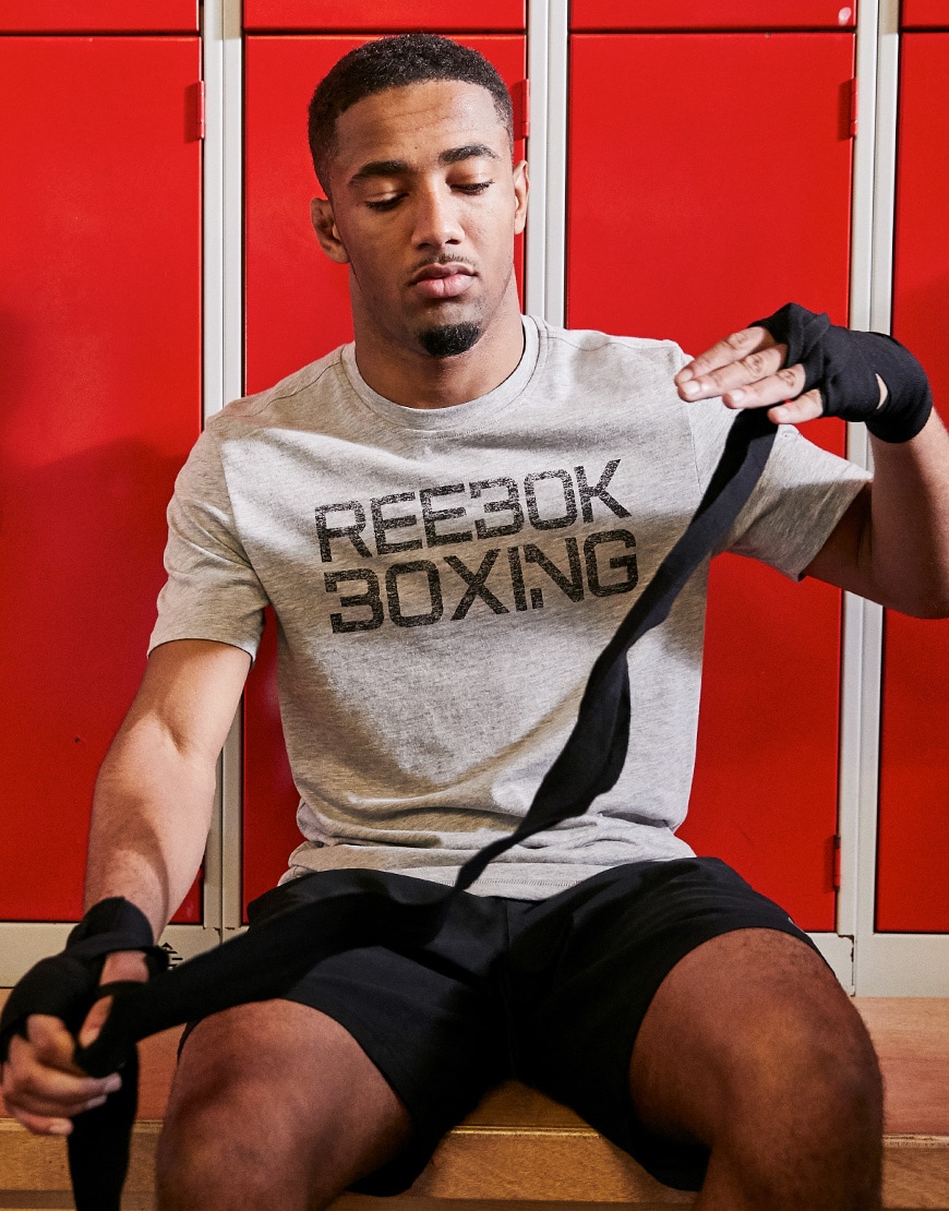 A picture of a man getting ready to go to the gym wearing a grey Reebok T-shirt and black shorts. Both Available on ASOS.