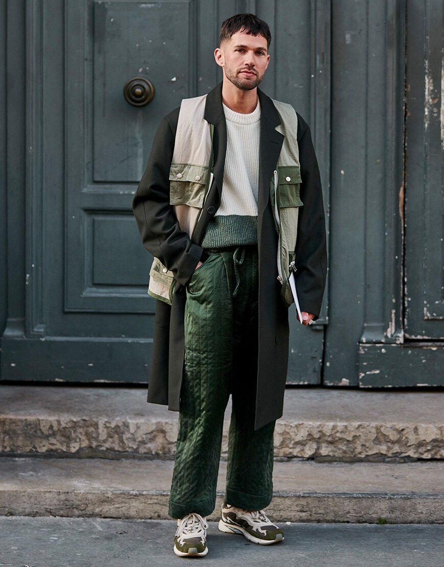 A street-styler at Paris Fashion Week Men's wearing a layered, all-green outfit, featuring a lightweight gilet on top of an overcoat | ASOS Style Feed 