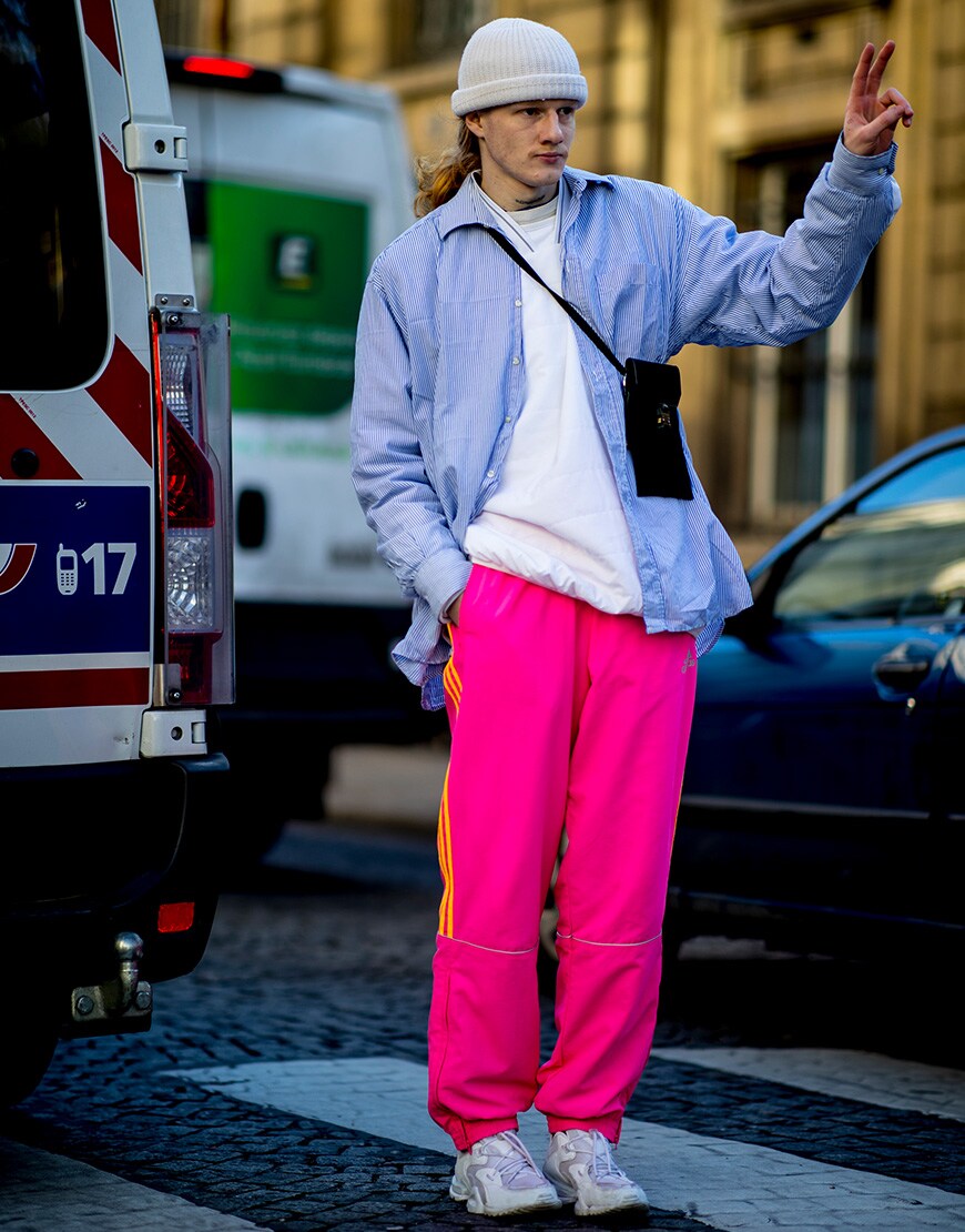 A street-styler at Paris Fashion Week Men's wearing highlighter pink tracksuit bottoms, a bright blue shirt and tee and a white beanie | ASOS Style Feed