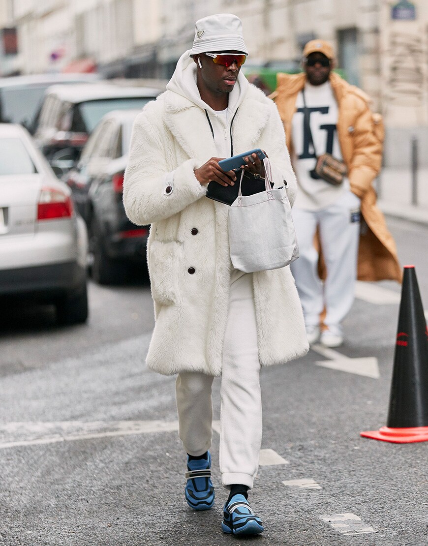 A street-styler at Paris Fashion Week Men's wearing an all-white outfit, featuring a bucket hat, hoodie, cuffed trousers and techy trainers | ASOS Style Feed