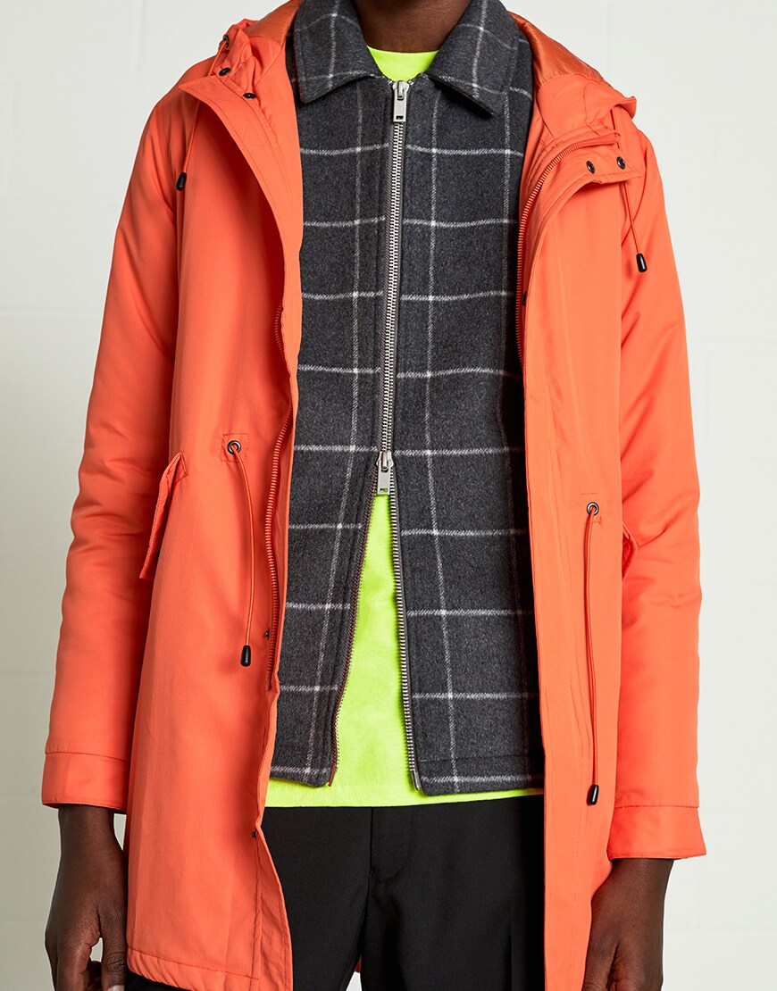 A close up picture of an orange coat with a check zip-up jacket and neon green T-shirt underneath. Available at ASOS.