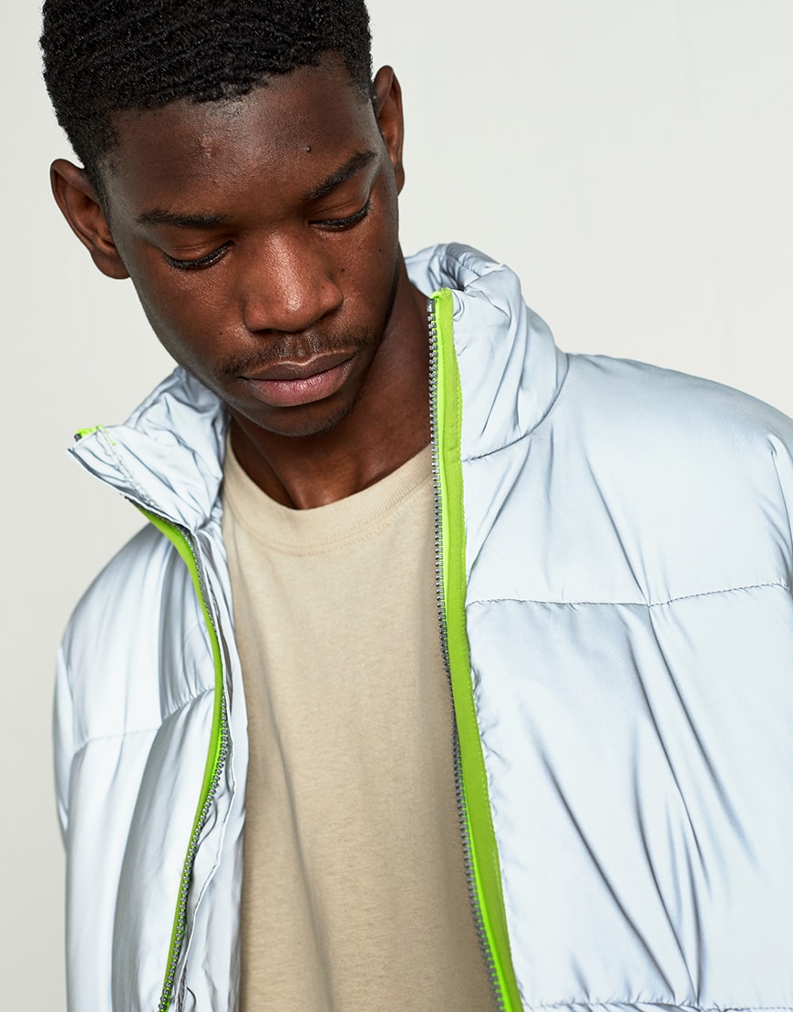 A close up picture of a reflective puffer jacket with neon green zip detail.
