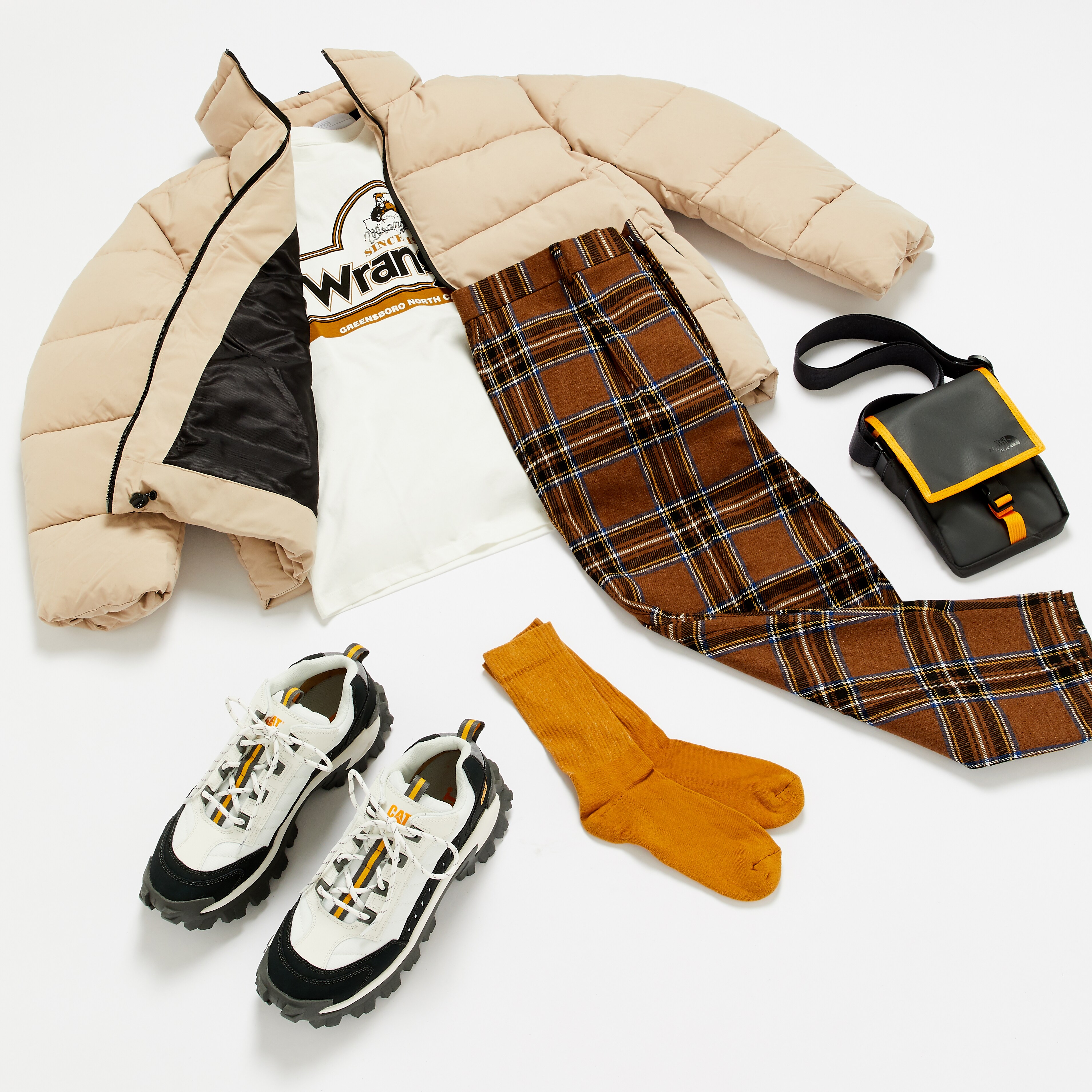 A picture of a streetwear-inspired outfit featuring a puffer jacket, Wrangler sweatshirt, CAT trainers, check trousers and accessories.