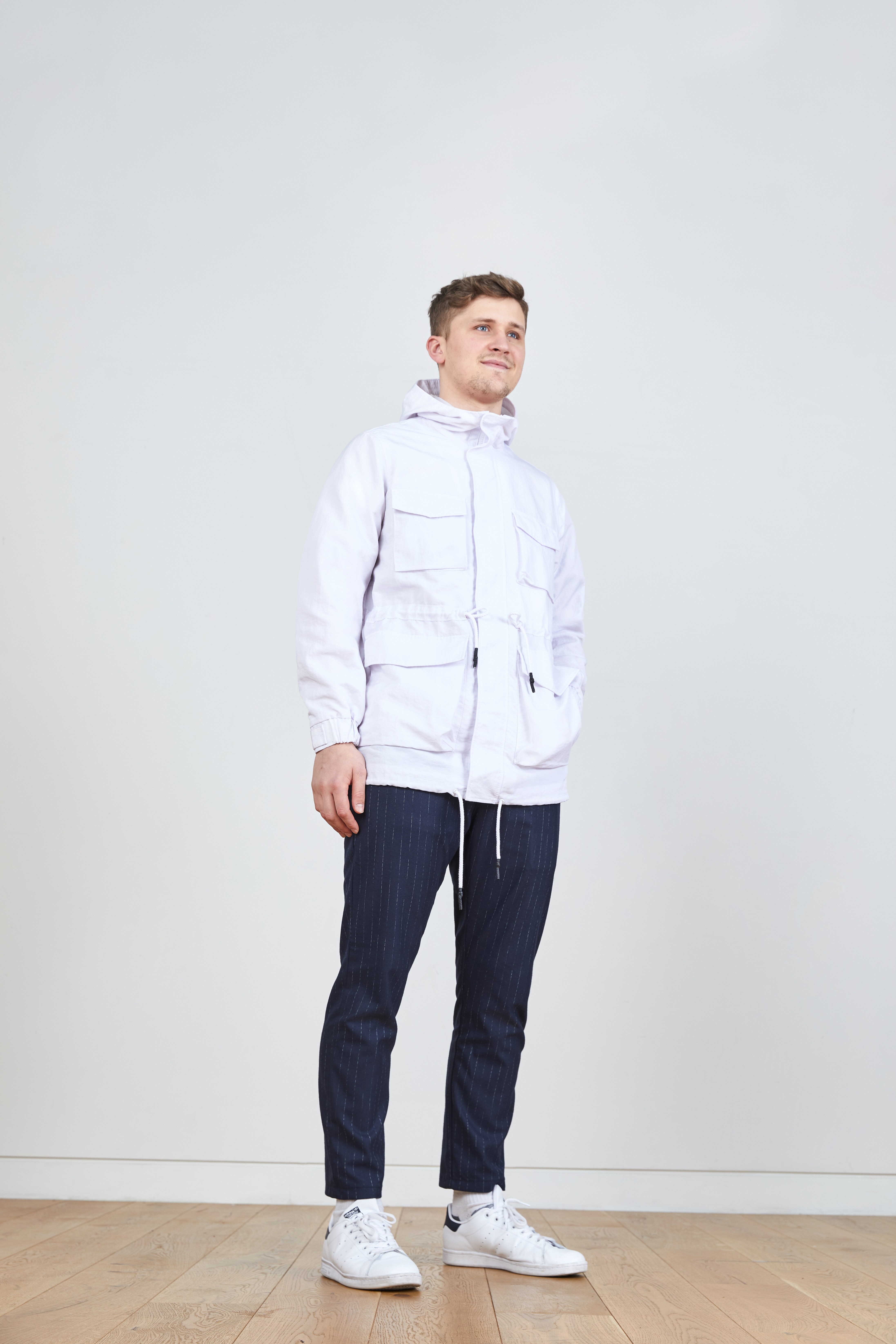 A picture of a man wearing a white, lightweight jacket from ASOS with pinstripe trousers and white trainers.
