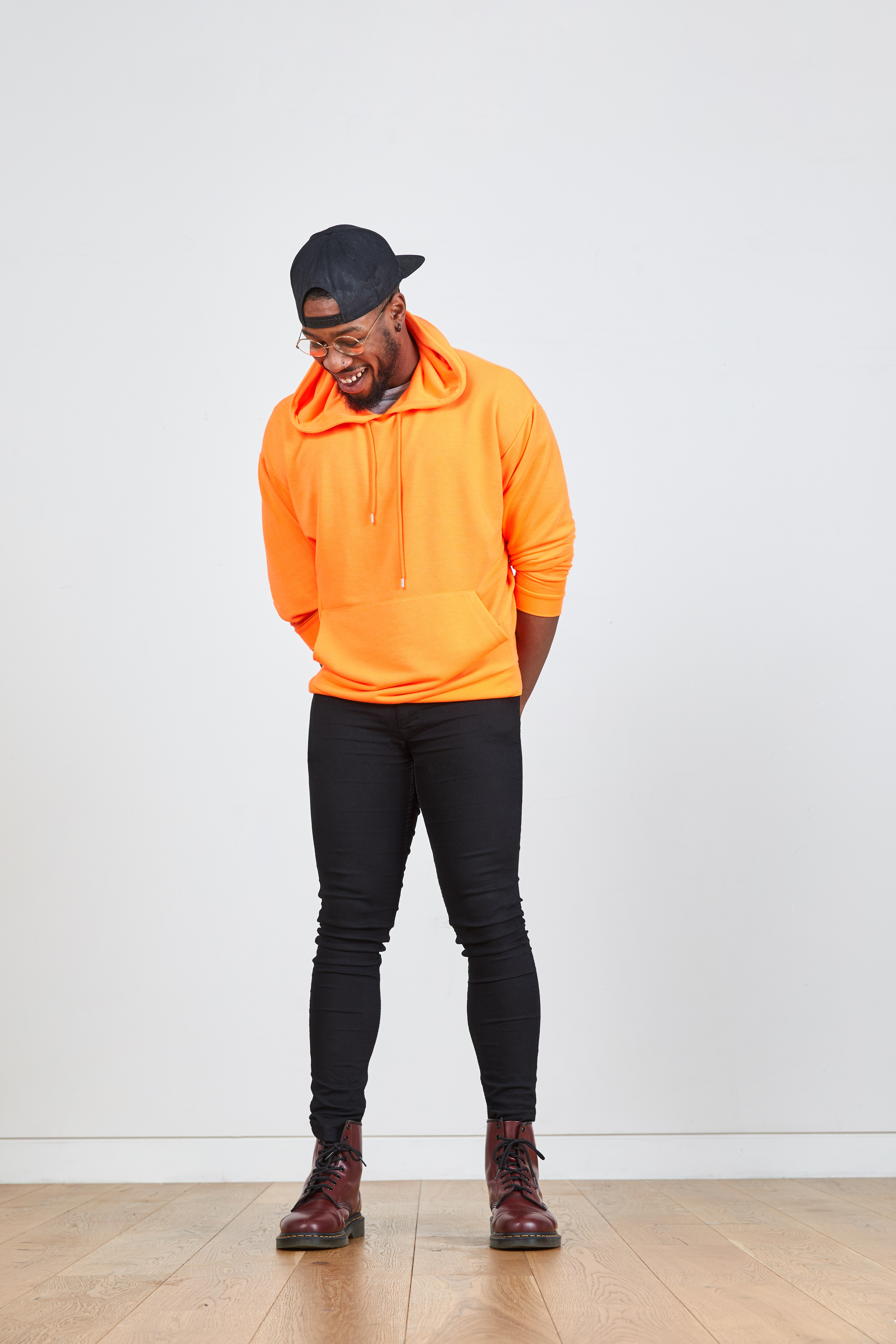 A picture of a man wearing a neon orange hoodie, black skinny jeans and a black cap.