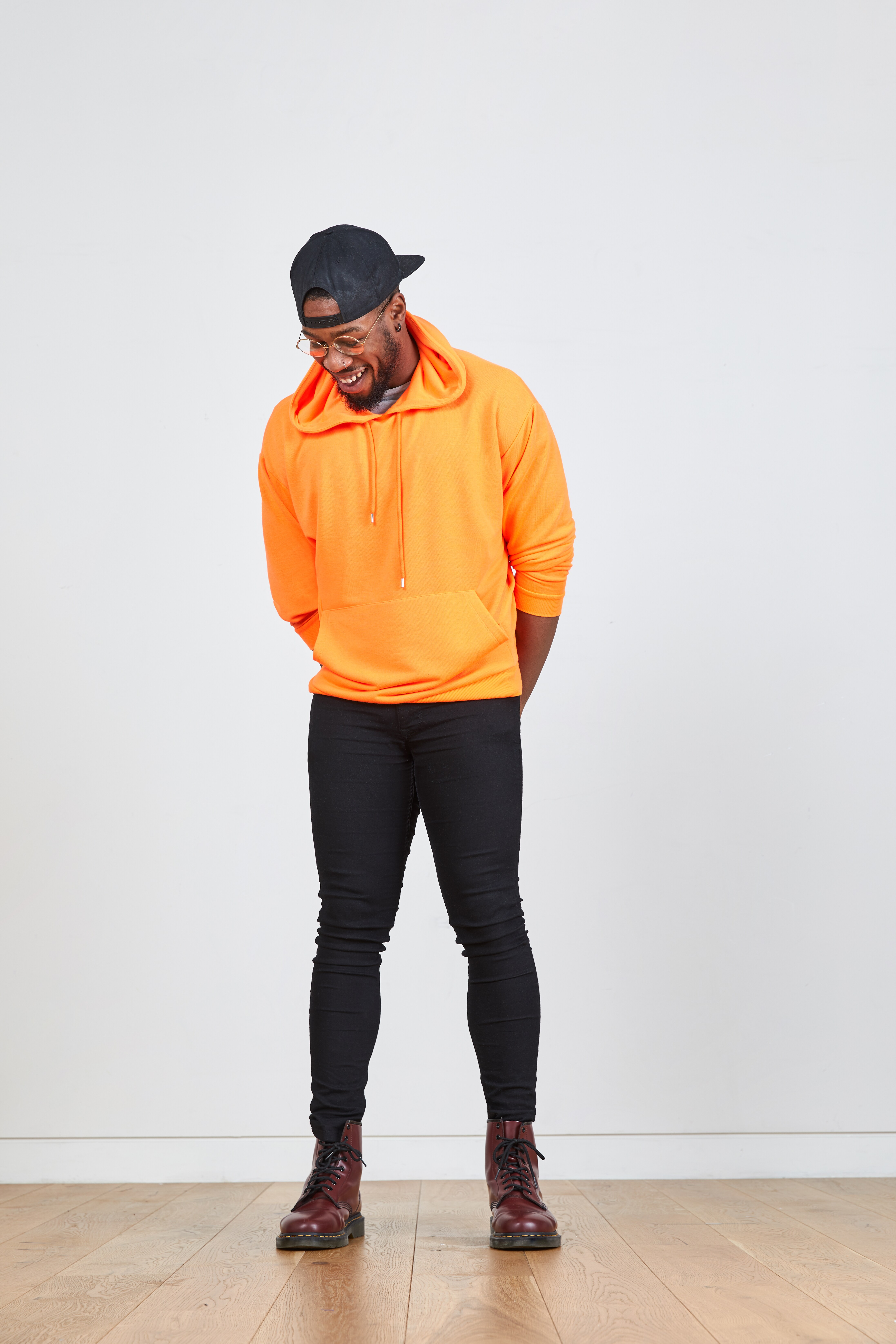 A picture of a man wearing a neon orange hoodie, black skinny jeans and a black cap.