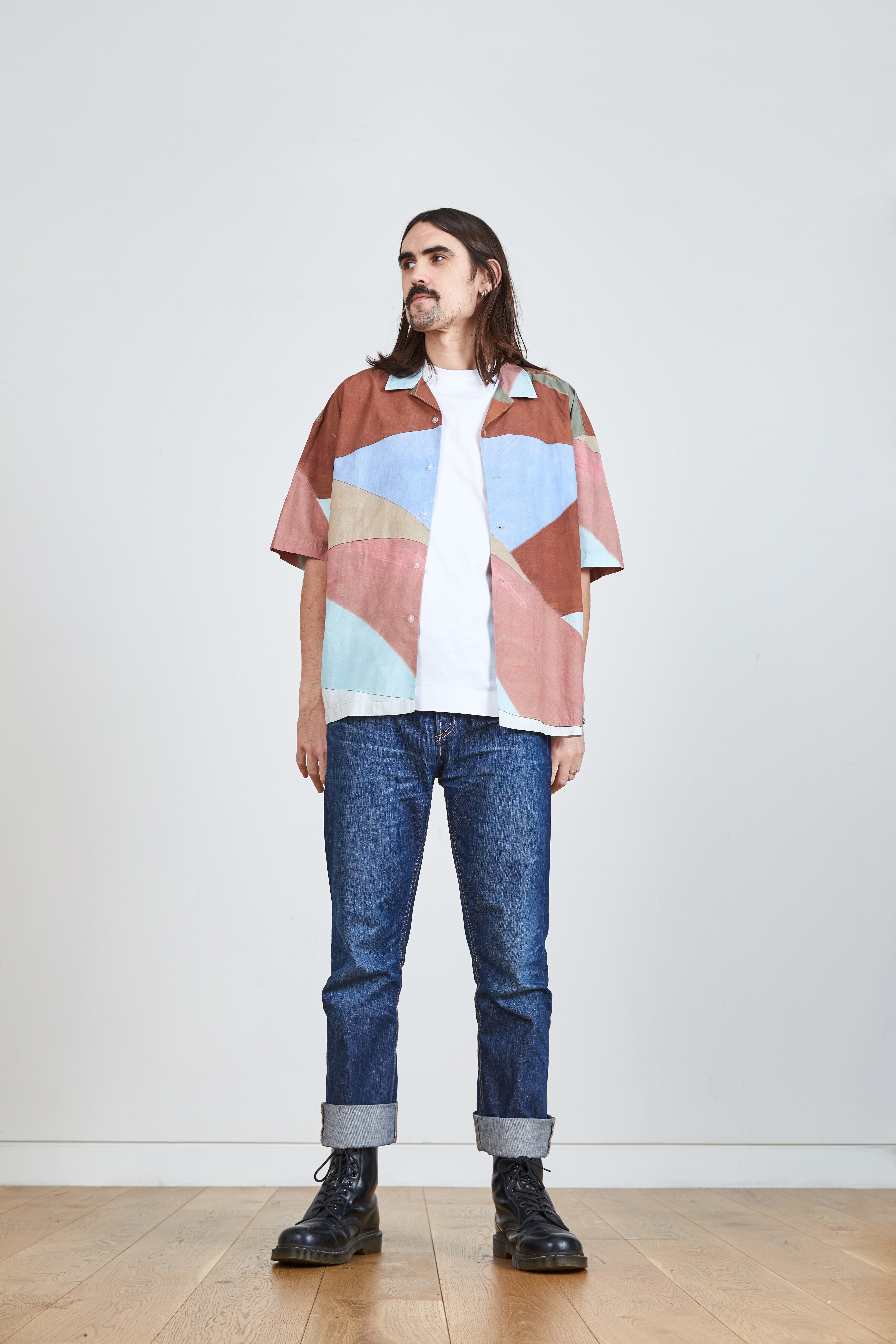 A picture of a man wearing a multi-colour short sleeve shirt with dark blue selvedge jeans and black Dr Martens boots.