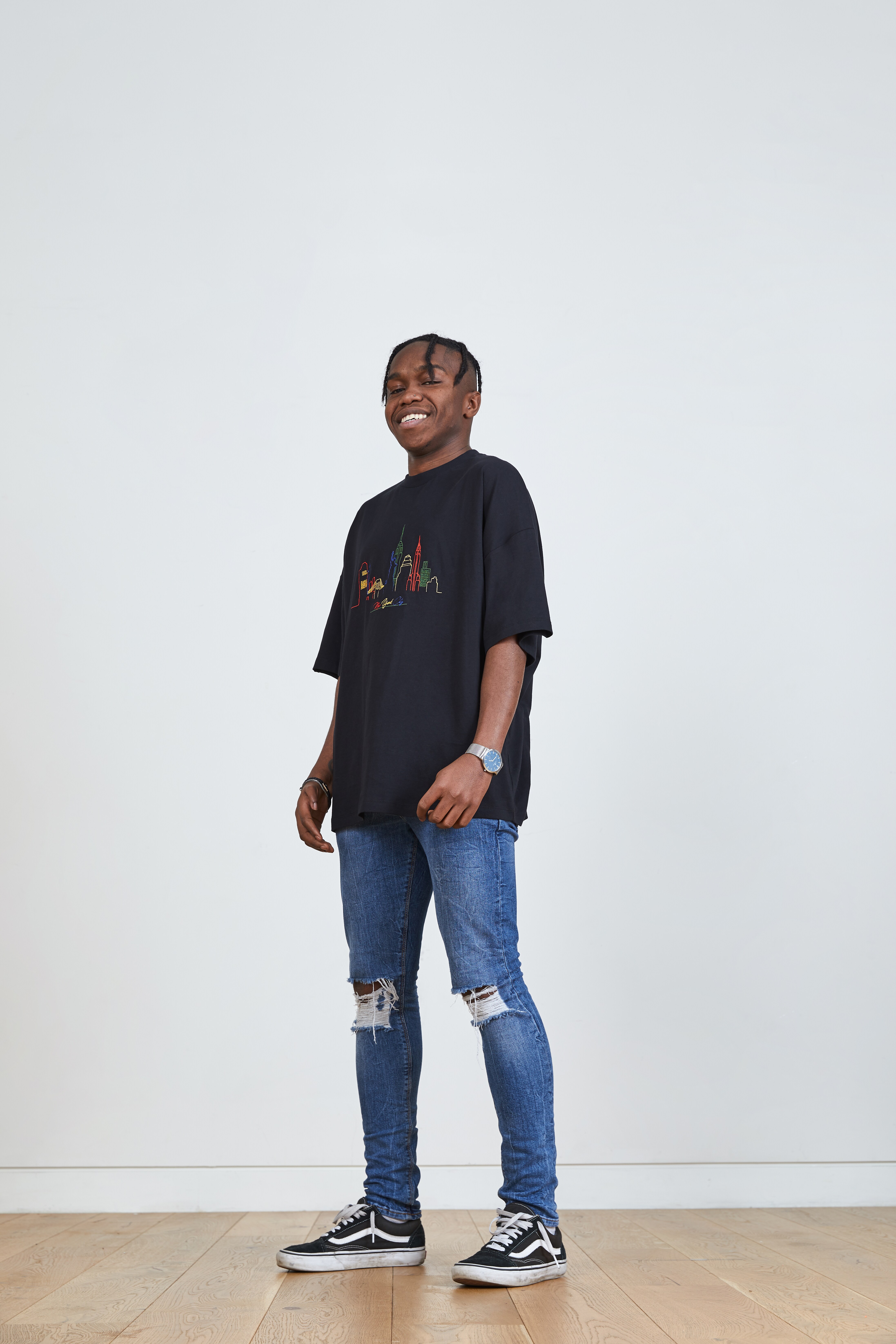 A picture of a man wearing a black T-shirt with multi-coloured embroidery and blue, ripped skinny jeans.