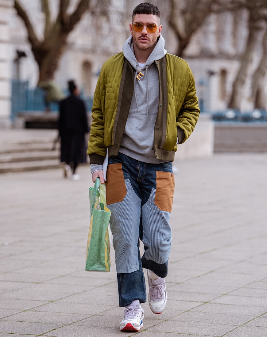 A picture of a streetstyler wearing a bomber jacket and hoodie with patchwork jeans.
