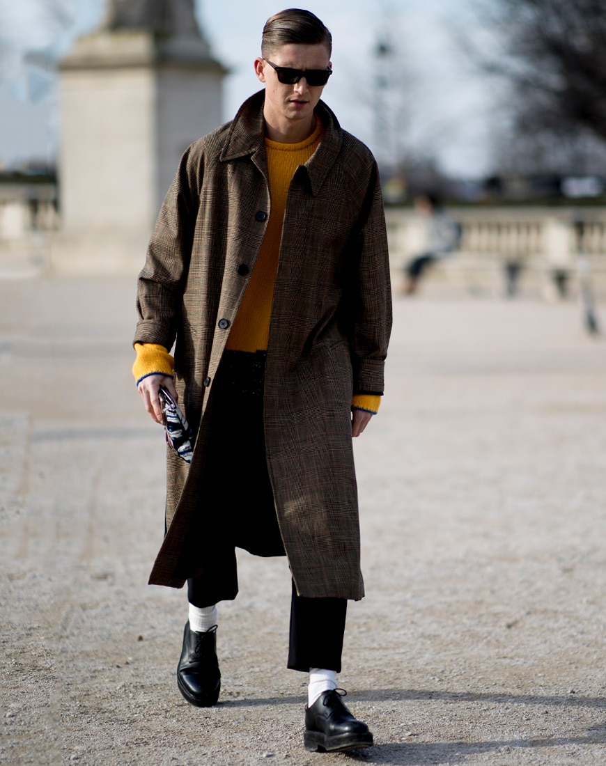 A picture of a streetstyler wearing a check trench coat with a yellow jumper.