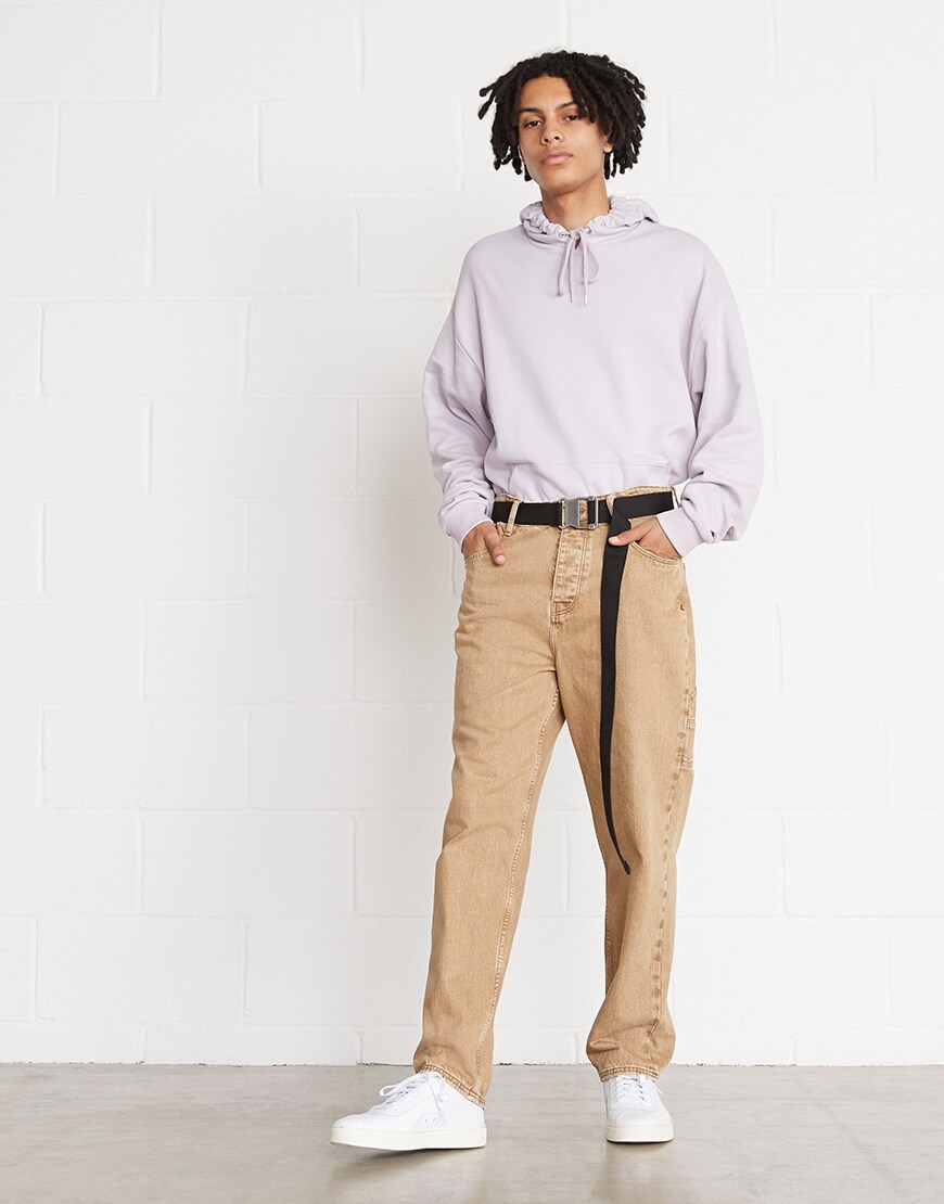 Une photo d'un modèle portant un sweat à capuche violet délavé, un jean beige et des baskets blanches. Disponible chez ASOS.