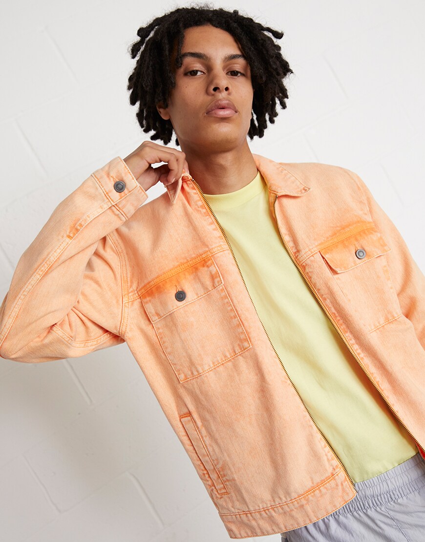 A picture of a model wearing a washed-orange denim jacket with Nike tracksuit bottoms and trainers. Available at ASOS.
