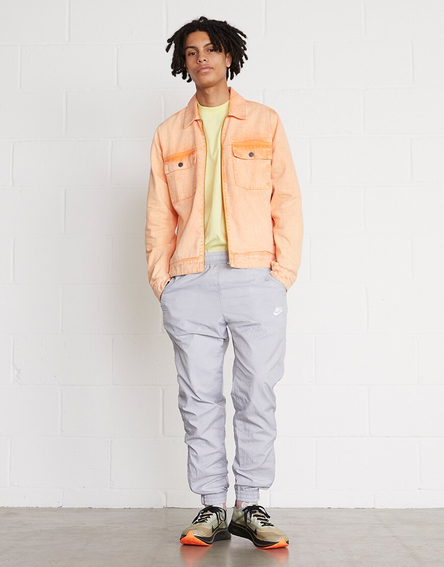 A picture of a model wearing a washed-orange denim jacket with Nike tracksuit bottoms and trainers. Available at ASOS.
