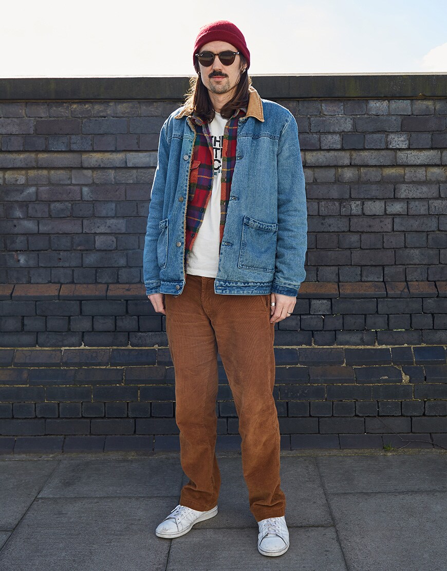 A picture of an ASOSer wearing a denim overshirt, check shirt, cord trousers and a red beanie.