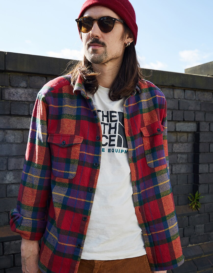 A picture of an ASOSer wearing a check shirt, a T-shirt from The North Face, a red beanie and Ray Ban sunglasses.