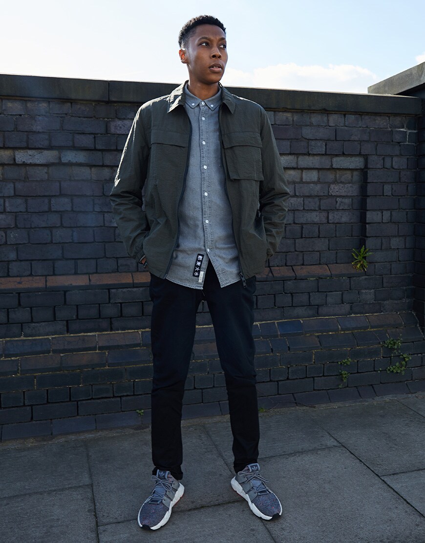 A picture of an ASOSer wearing a coach jacket, a denim shirt and black trousers.