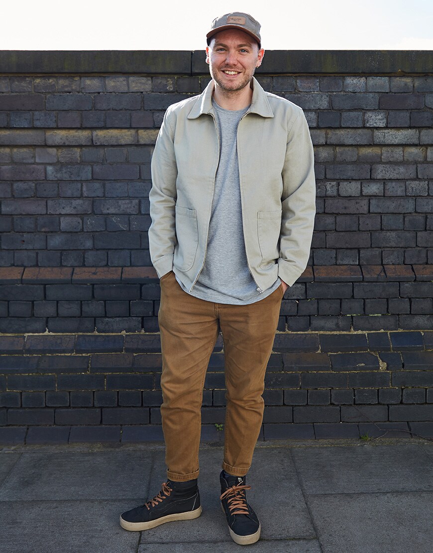 A picture of an ASOSer wearing a cap and overshirt with tan-coloured trousers and Vans trainers.