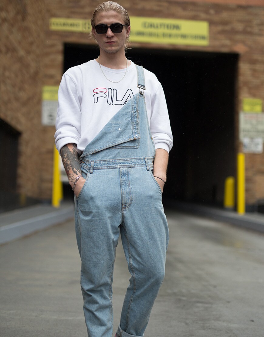 A picture of a street styler wearing denim dungarees with a Fila sweatshirt.