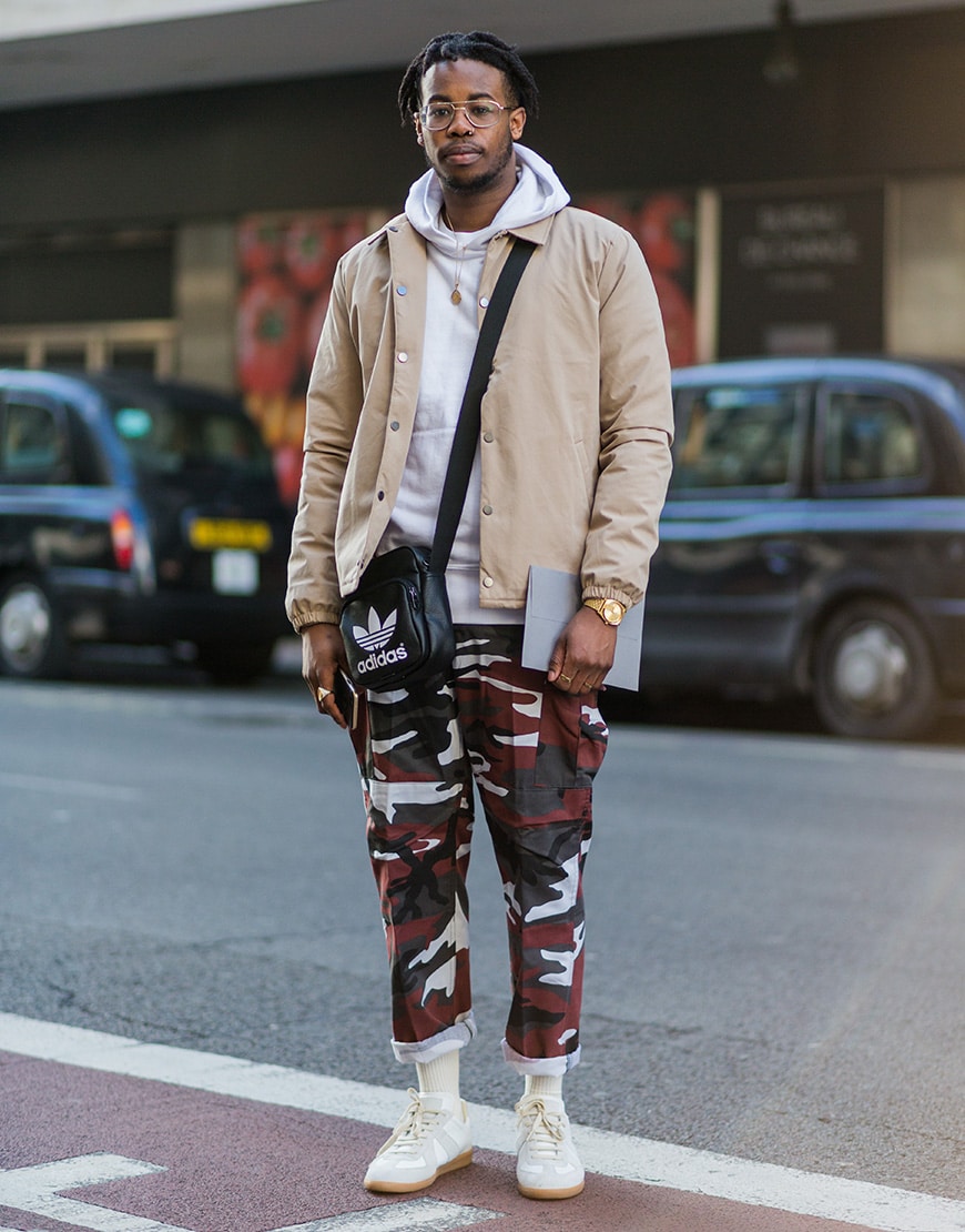 A street styler wearing a coach jacket and hoodie with a pair of camo-print trousers.