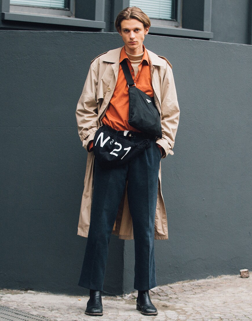 A street styler wearing a lightweight trench coat with a shirt and smart trousers.
