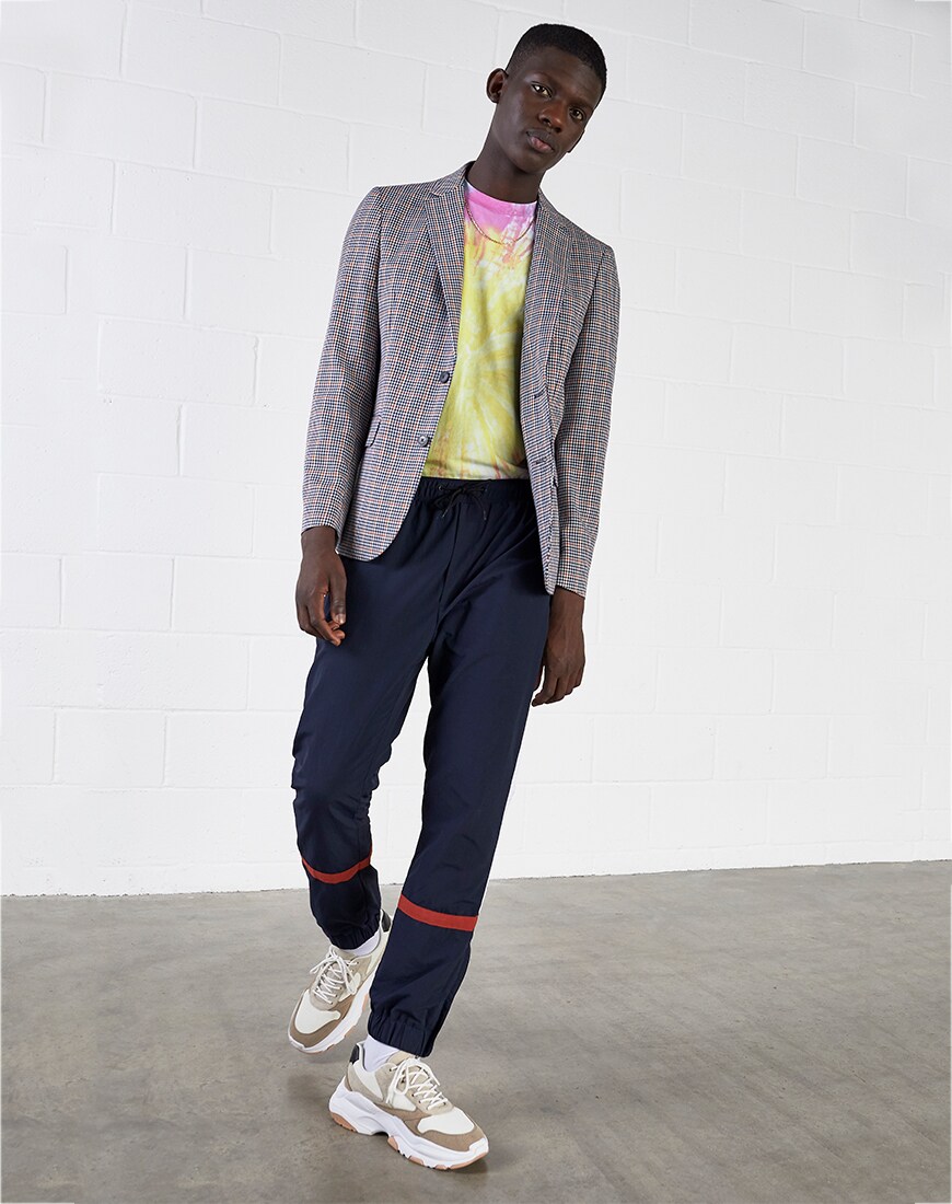 A picture of a model wearing a tie-dye T-shirt with a blazer, sweatpants and chunky trainers. Available at ASOS.