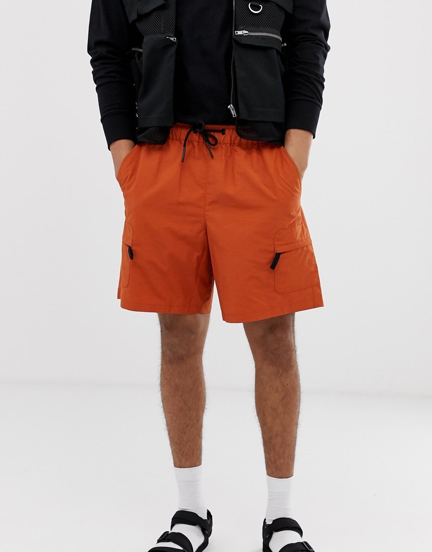 A picture of a model wearing a pair of orange utility-style shorts. Available at ASOS.