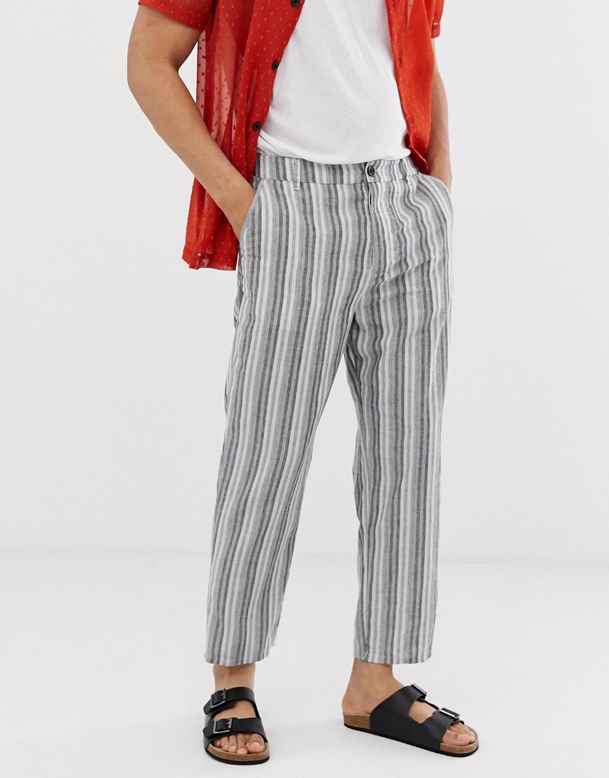 A picture of a model wearing a pair of linen trousers in a grey stripe design. Available at ASOS.
