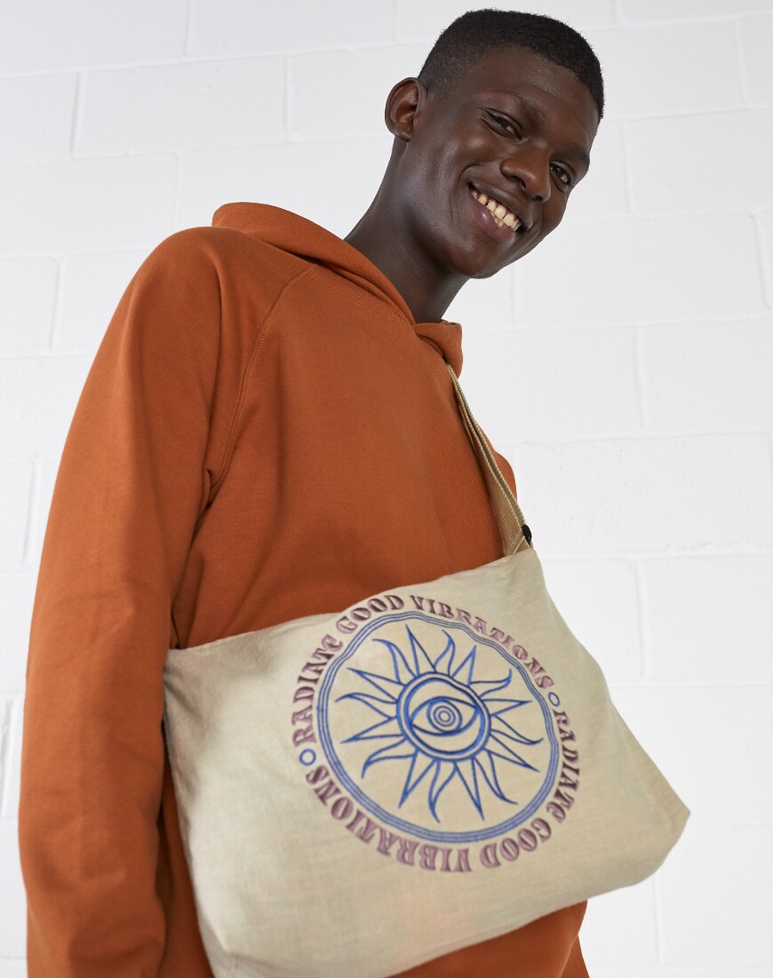 A close-up picture of a model wearing a rust-coloured hoodie and an embroidered satchel. Available at ASOS.